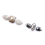 Assorted natural salt and pepper and white rustic diamonds in pear, hexagon, and elongated geometric cuts displayed on a white background, featuring visible inclusions and raw organic patterns.