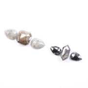 Assorted natural salt and pepper and white rustic diamonds in pear, hexagon, and elongated geometric cuts displayed on a white background, featuring visible inclusions and raw organic patterns.