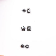 Six natural black diamonds in geometric cuts including star, kite, emerald rectangle, pentagon, and round brilliant shapes displayed on white background.