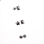 Six natural black diamonds in geometric cuts including star, kite, emerald rectangle, pentagon, and round brilliant shapes displayed on white background.
