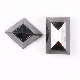Pair of natural black diamonds featuring a shield-shaped cut and an elongated baguette-style cut, loose matching set with faceted surfaces for custom fine jewelry design.