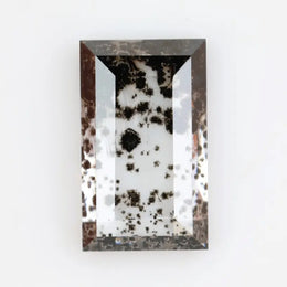 Rectangular step cut lab grown diamond featuring dramatic black dendritic inclusions in a salt and pepper pattern, creating a unique one of a kind modern alternative diamond with striking natural looking carbon formations inside a clear faceted stone.