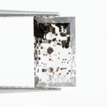 Rectangular step cut lab grown diamond featuring dramatic black dendritic inclusions in a salt and pepper pattern, creating a unique one of a kind modern alternative diamond with striking natural looking carbon formations inside a clear faceted stone.