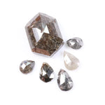 Set of natural salt and pepper diamonds including one hexagon cut center stone and five pear-shaped diamonds with visible inclusions and earthy brown, gray, and translucent tones on white background.