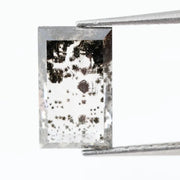 Rectangular step cut lab grown diamond featuring dramatic black dendritic inclusions in a salt and pepper pattern, creating a unique one of a kind modern alternative diamond with striking natural looking carbon formations inside a clear faceted stone.