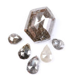 Set of natural salt and pepper diamonds including one hexagon cut center stone and five pear-shaped diamonds with visible inclusions and earthy brown, gray, and translucent tones on white background.