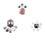 Assorted natural fancy color diamonds including salt and pepper hexagon cut, pear rose cuts, peach oval, dark geometric step cut center stone, and small pyramid-cut accent diamonds arranged on white background.