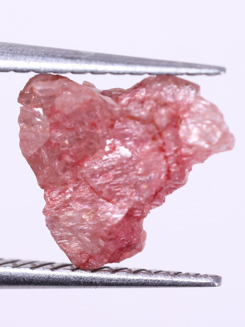Raw pink diamond held by tweezers on a white background