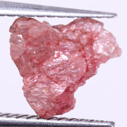 Raw pink diamond held by tweezers on a white background