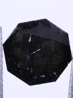 Black octagon lab grown between two tweezers on a black background