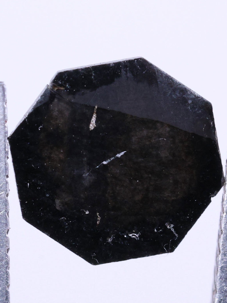 Black octagon lab grown between two tweezers on a black background