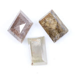 Three natural diamonds including a pink included fancy cut diamond, a golden brown heavily included diamond, and a clear step cut rectangular natural diamond displayed on a white background.