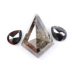 Natural salt and pepper trillion cut diamond with visible inclusions, flanked by two pear shaped black diamonds on white background