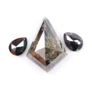 Natural salt and pepper trillion cut diamond with visible inclusions, flanked by two pear shaped black diamonds on white background