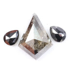 Natural salt and pepper trillion cut diamond with visible inclusions, flanked by two pear shaped black diamonds on white background