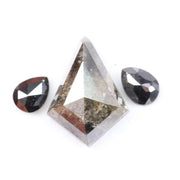 Natural salt and pepper trillion cut diamond with visible inclusions, flanked by two pear shaped black diamonds on white background