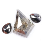 Natural salt and pepper trillion cut diamond with visible inclusions, flanked by two pear shaped black diamonds on white background
