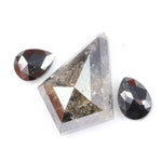 Natural salt and pepper trillion cut diamond with visible inclusions, flanked by two pear shaped black diamonds on white background