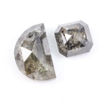 Pair of natural salt and pepper diamonds featuring a half moon rose cut and an octagonal step cut, both with visible grey and black inclusions and a rustic translucent appearance on a white background.