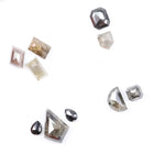 Assorted natural salt and pepper diamonds in geometric fancy cuts including kite, shield, emerald, pear, half moon, and octagon shapes in earthy tones of grey, champagne, cognac, and blush with visible natural inclusions.