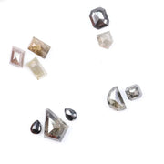 Assorted natural salt and pepper diamonds in geometric fancy cuts including kite, shield, emerald, pear, half moon, and octagon shapes in earthy tones of grey, champagne, cognac, and blush with visible natural inclusions.