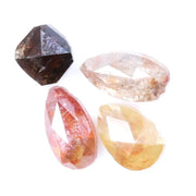 Collection of natural fancy color diamonds including pink, yellow, champagne and cognac loose diamonds with faceted cuts displayed on white background for fine jewelry and gemstone collecting.