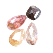 Collection of natural fancy color diamonds including pink, yellow, champagne and cognac loose diamonds with faceted cuts displayed on white background for fine jewelry and gemstone collecting.