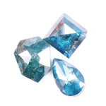 Collection of natural blue diamonds in unique geometric cuts including triangular, hexagon, and pear shapes with vivid ocean-blue tones and natural inclusions on a white background.