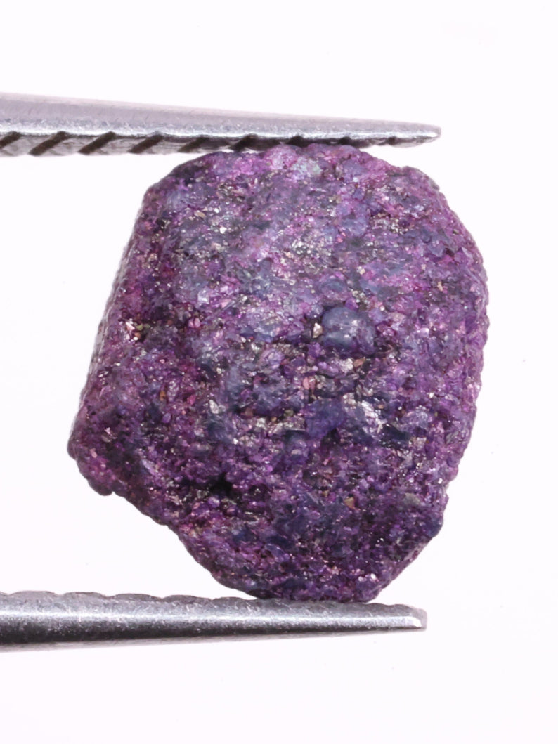 Purple rough diamond held between tweezers on a white background