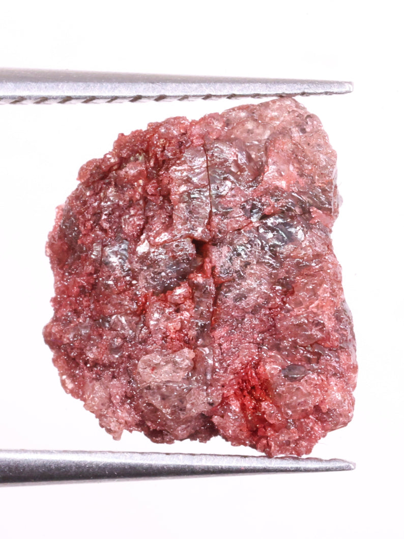 Raw light red diamond held by tweezers on a white background