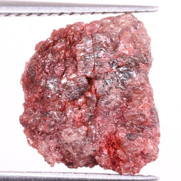 Raw light red diamond held by tweezers on a white background