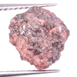 Raw light pink diamond held between tweezers on a white background