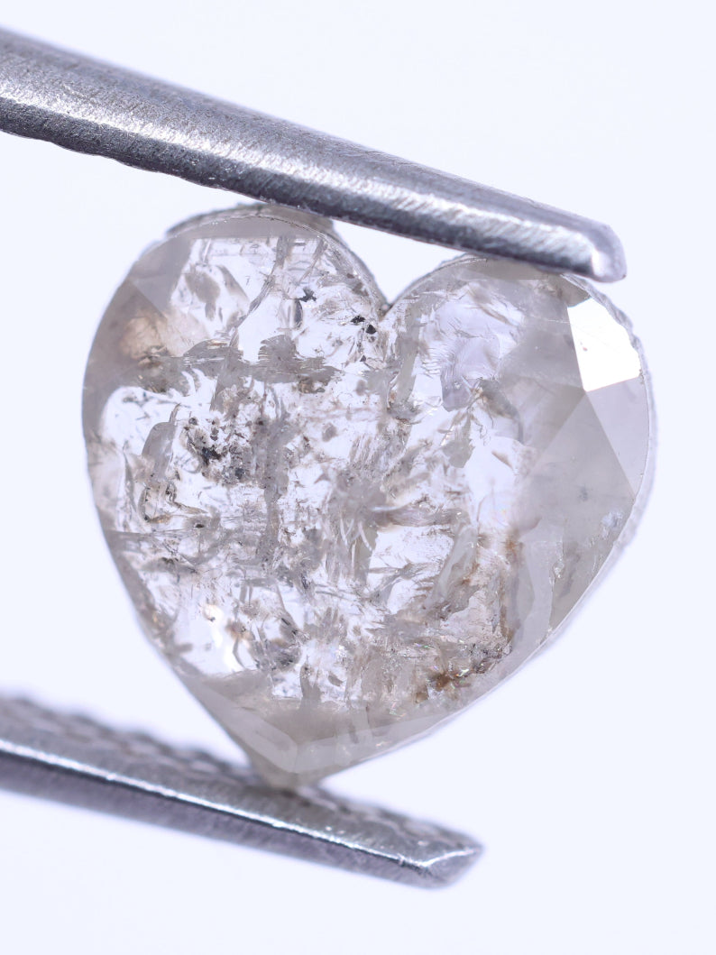 Heart-shaped diamond held by tweezers on a white background