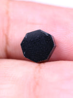 Black stone held between fingers on a light skin background