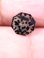 Octagon stone with a spotted pattern held between fingers on a light balck background