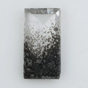 Baguette cut lab grown diamond with salt and pepper inclusions, showcasing a unique speckled galaxy pattern inside a clear faceted rectangular stone on a white background