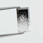 Baguette cut lab grown diamond with salt and pepper inclusions, showcasing a unique speckled galaxy pattern inside a clear faceted rectangular stone on a white background