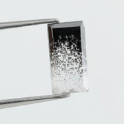 Baguette cut lab grown diamond with salt and pepper inclusions, showcasing a unique speckled galaxy pattern inside a clear faceted rectangular stone on a white background