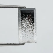 Baguette cut lab grown diamond with salt and pepper inclusions, showcasing a unique speckled galaxy pattern inside a clear faceted rectangular stone on a white background