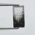 Baguette cut lab grown diamond with salt and pepper inclusions, showcasing a unique speckled galaxy pattern inside a clear faceted rectangular stone on a white background