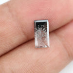 Baguette cut lab grown diamond with salt and pepper inclusions, showcasing a unique speckled galaxy pattern inside a clear faceted rectangular stone on a white background