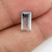 Baguette cut lab grown diamond with salt and pepper inclusions, showcasing a unique speckled galaxy pattern inside a clear faceted rectangular stone on a white background