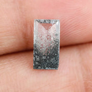 Baguette cut lab grown diamond with salt and pepper inclusions, showcasing a unique speckled galaxy pattern inside a clear faceted rectangular stone on a white background
