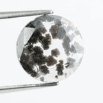Round cut lab grown salt and pepper diamond featuring bold black dendritic inclusions in a transparent stone, faceted for brilliance and showcasing a unique natural pattern