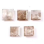 Five square step cut champagne lab grown diamonds with galaxy salt and pepper inclusions, pyramid faceting, and rustic brown tones displayed on a white background.