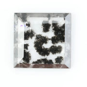 Clear lab-grown diamond with striking black natural-style inclusions inside a polished rectangular crystal, showcasing a unique modern gemstone aesthetic