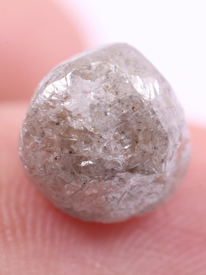 Raw diamond held between fingers against a neutral background