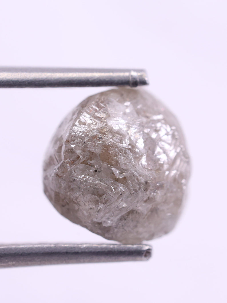 Raw diamond held between tweezers on a white background