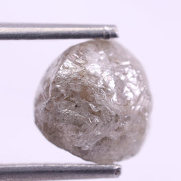Raw diamond held between tweezers on a white background