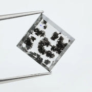 Clear lab-grown diamond with striking black natural-style inclusions inside a polished rectangular crystal, showcasing a unique modern gemstone aesthetic